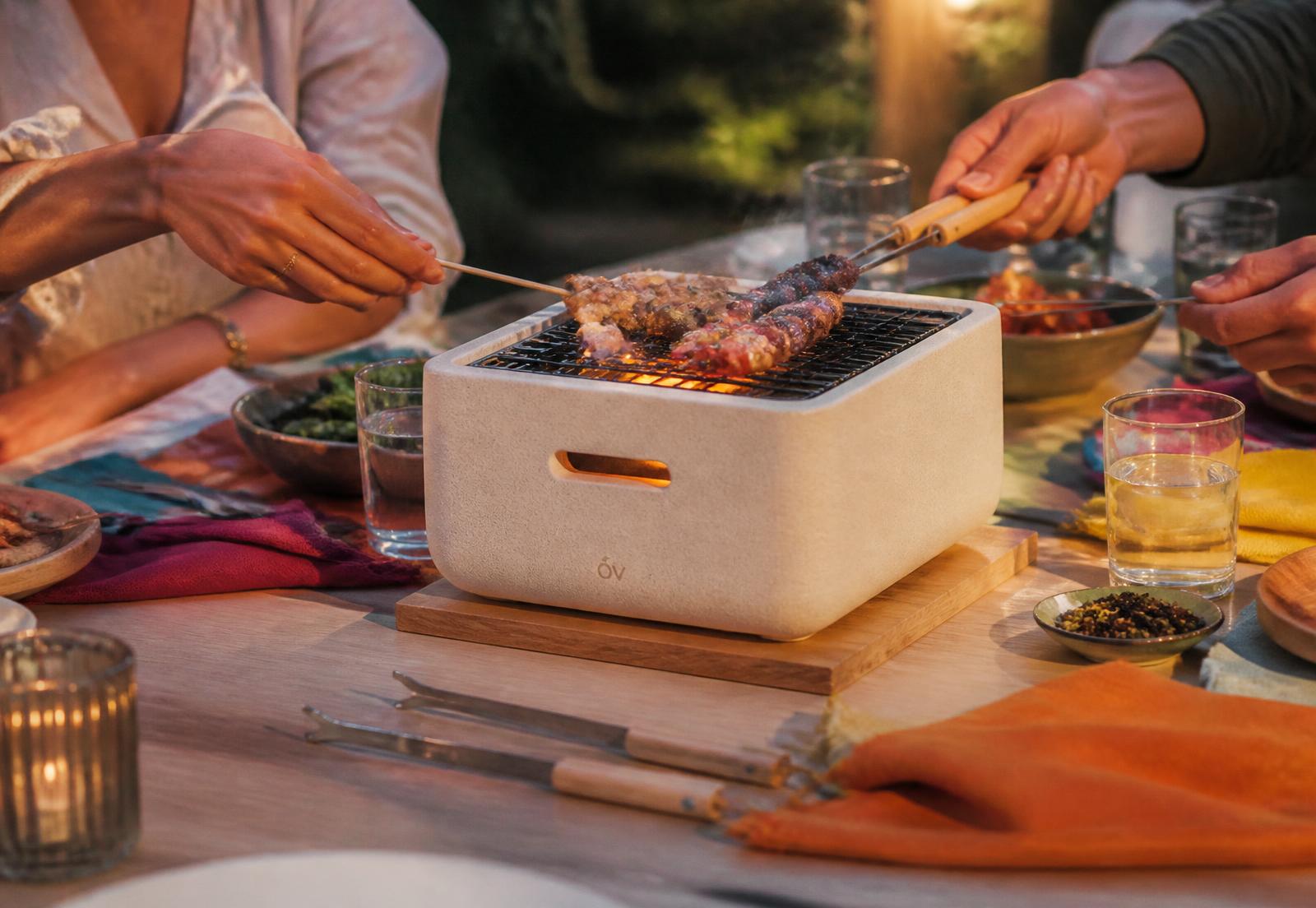 Mini-grill en céramique posé au centre d'une table, brochettes en train de cuire