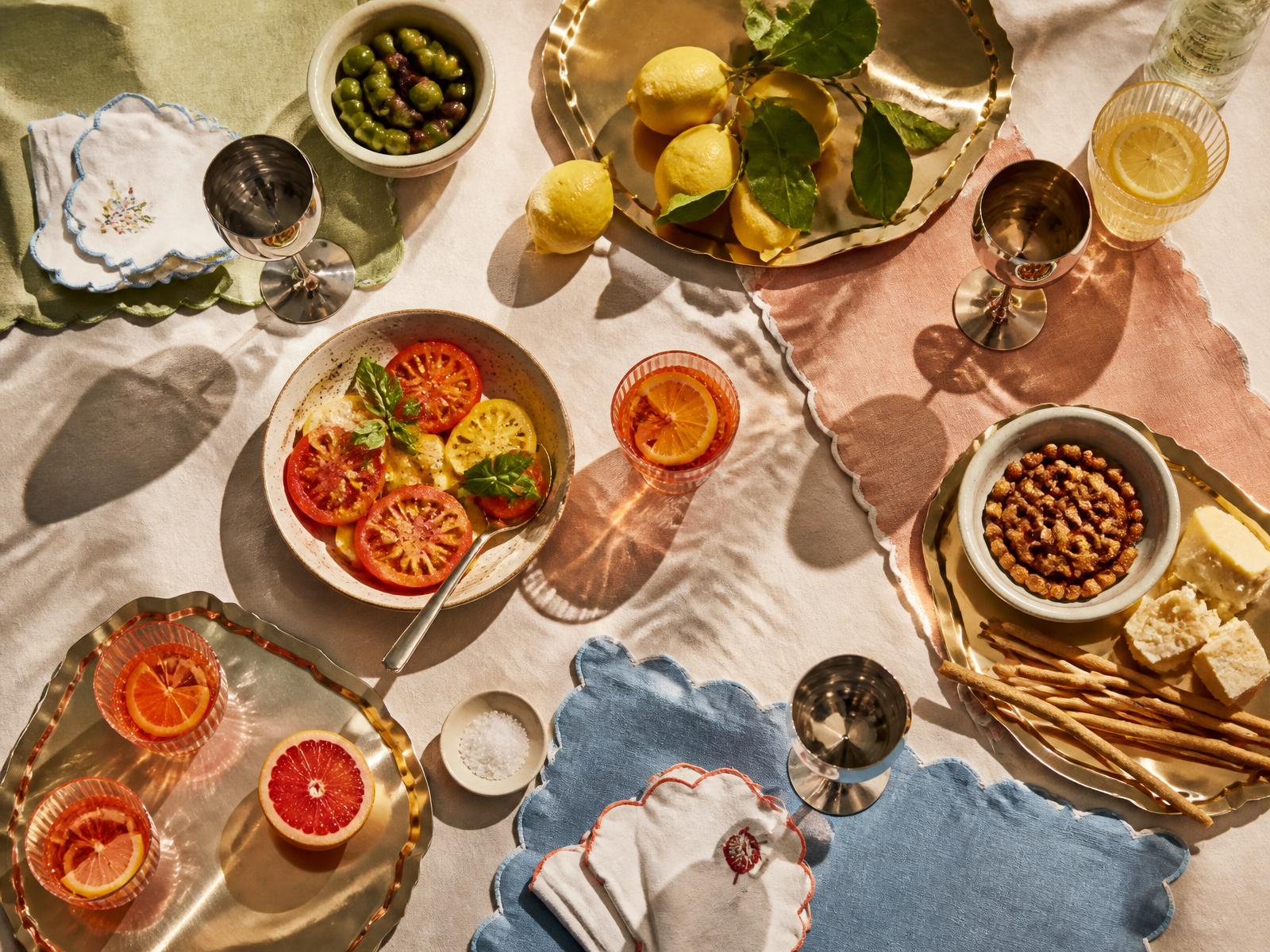 Vue de dessus d'une table d'apéro : lin coloré, plateaux champagne, céramique, olives, citrons et cocktails
